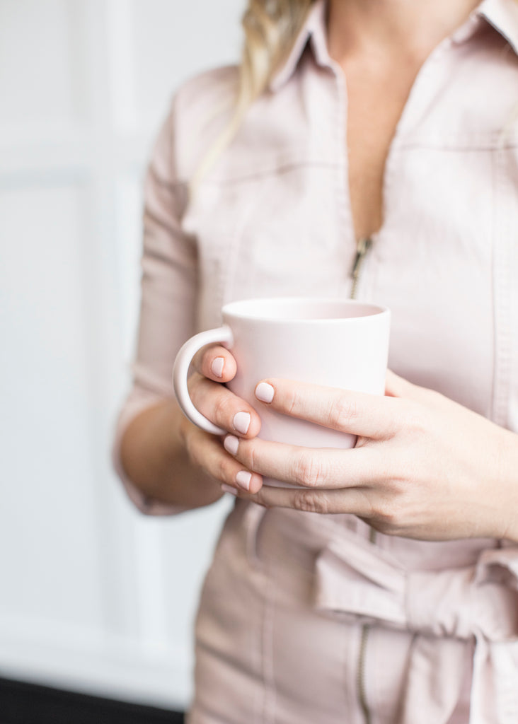 woman with blonde hair in pink suit holding a white coffee cup