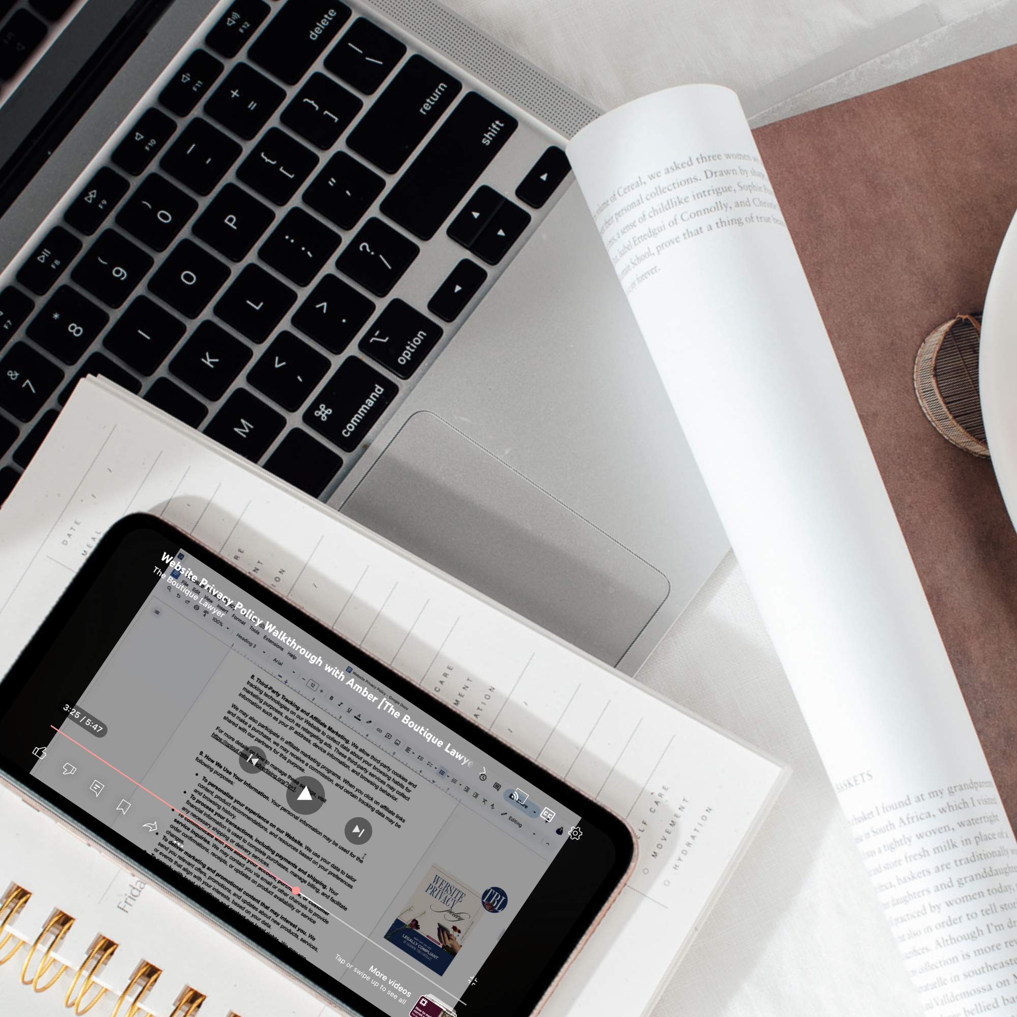 Website policy legal template video walkthrough on a phone laying on a desktop with a laptop and attorney-drafted notes to protect the websites of creative entrepreneurs.